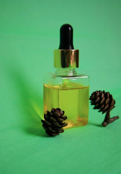 緑の背景に小さなコーンの横にあるドロッパーボトルに油を針葉樹 松精油 杉のトウヒ油 有機天然化粧品 スパのウェルネストリートメント 薬剤の概念 垂直写真 — ストック写真