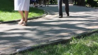 Güneşli yaz günlerinde şehir parkında yürüyen tanınmamış insanlar. Farklı insanların ayakları yeşil çimlerle kaplı bahçede fayanslı bir patikada geziniyor. Doğada, bir sokakta dinleniyor.. 