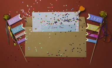 Aşk mektubu. Terra cotta arka planında Sevgililer Günü aşk notu olan kahverengi bir zarf. Renkli konfeti, bayraklar, kalp. 14 Şubat üst görünümü için kutlama kartı.