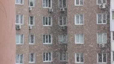 Apartman penceresinden bir ev manzarası. Soğuk kış mevsiminde gündüz vakti açık havada kar taneleri düşüyor. Çok katlı bir tuğla binanın birçok penceresi. Şehirde kar fırtınası. Şehir hayatı