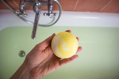 Sarı banyo bombasını suya koyan bir kadın eli. Elinde deniz tuzu olan kavun kokulu bir bomba küvet dolusu suya karşı. Spa yap ve evde dinlen. Boşluğu kopyala, metin için yer.