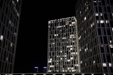 Kyiv, Ukrayna. Karanlık bir gökyüzüne karşı arka ışıklandırması olan modern çok katlı binalar. Geceleri pencerelerde ışıklar yanar. Şehir mimarisi. Aydınlanmış evler.