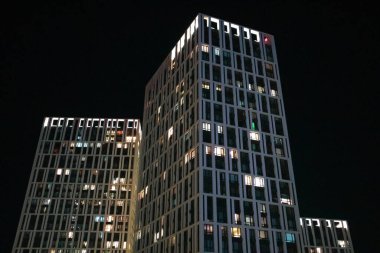Kyiv, Ukrayna. Karanlık bir gökyüzüne karşı arka ışıklandırması olan modern çok katlı binalar. Geceleri pencerelerde ışıklar yanar. Şehir mimarisi. Aydınlanmış evler.