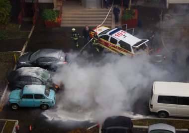 Kyiv, Ukrayna. 7 Ekim 2021. İtfaiyeciler apartmanın bahçesine park etmiş yanan arabayı söndürüyorlar. Acil durum. Sigorta olayı. Duman bulutları, kaputun altından çıkan alevler.