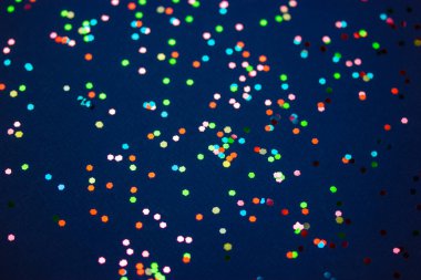 Çok renkli konfeti koyu mavi yüzey manzarasına saçılmış. Bir sürü yuvarlak pul. Kutlama, parti, eğlence konsepti. Eğlenceli soyut şenlik arkaplanı. Dekorasyon için parıldayan küçük elementler.