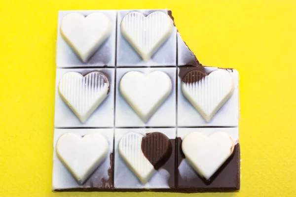 Milky dark chocolate bar with hearts on each slice top view. Broken black white pieces on yellow background flatly. World Chocolate Day. Sweet, calorie unhealthy food. Valentine\'s day and love concept