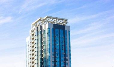 Güneşli bir günde mavi bulutlu bir gökyüzüne karşı modern bir apartman. Büyük şehirde simetrik modern mimarisi olan bir apartman dairesi. Gayrimenkul yatırımları, daire kiralama. İş merkezi