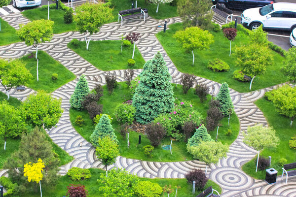 Landscape design concept. Greening area view from above. Green plants, grass, bushes, trees planted in a flowerbed. Pedestrian paved paths, stone walkway, the cars parked by a road. Spring garden.