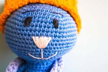 Mavi örgü örmüş, sarı şapkalı gülümseyen oyuncak kedi. Amigurumi sanatı. Childs 'ın eski oyuncak parçası. Yakın plan. Bebekler, yeni yürümeye başlayanlar ve çocuklar için yaratıcı el yapımı yumuşak bir oyuncak. Çocukluk kavramı
