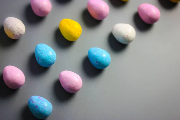 Multicolored bright Easter chocolate eggs yellow, white, pink, blue colors scattered on dark table background top view. Sweets and treats for children, kids in spring season holiday. Copy space — Stock Photo, Image