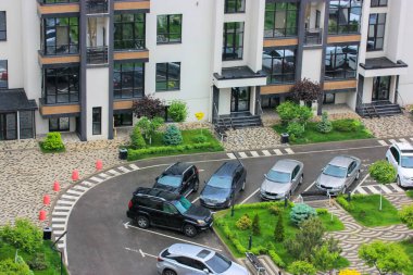 Modern apartman manzarasının avlusuna park edilmiş arabalar. Çok katlı bir ev ve güzel bir peyzaj. Otomobillerin park edildiği yeşil alan, kaldırımlar yayalar, yol işaretleri....