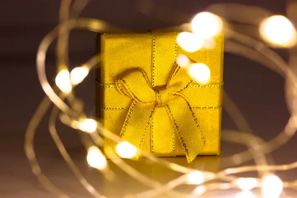 テーブルの上に弓のついた黄色いギフトボックスが輝く絡まったガーランドライトの中に立っています。2022年、クリスマス。魔法の冬の休日のショッピング。夕方にはプレゼント付きの金の箱。祭りの背景 — ストック写真