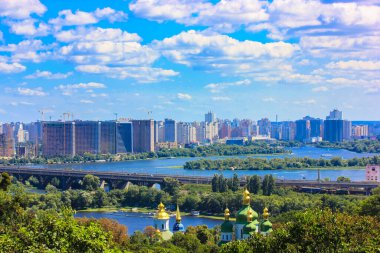 Kyiv, Ukrayna. 2 Mayıs 2021. Bir şehrin panoraması, güneşli bahar ve yaz günlerinde ağaçların yeşilliğine gömülmüş bir kasaba. Yüksek çok katlı konutlar. Nehir üzerindeki karayolu köprüsü Mavi gökyüzü, beyaz bulutlar.