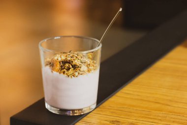 Doğal taze yoğurt ve Fransız tahıl gevreği, müsli, tahta masada kaşıkla cam bardakta yulaf ezmesi. Faydalı diyet yemek tarifi. Sağlıklı bir yaşam tarzı. Mısır gevreği kahvaltısı için tatlı yemek, dal. Metin için boşluk.