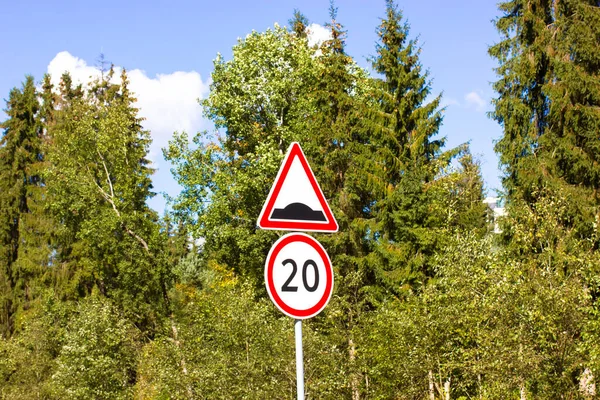 Two road signs for motorists warning about pedestrians and cyclists - speed limit to 20 kmh per hour, a sign of a speed bump on the background of green pine forests and blue sky. Caution speed bumps.