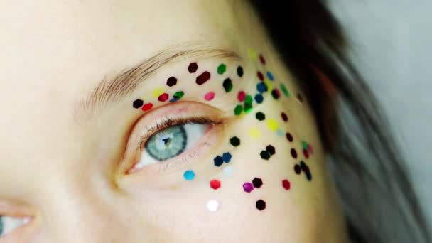 Mujer joven retrato énfasis en los ojos gris-azul con lentejuelas multicolores. Guiños — Vídeos de Stock