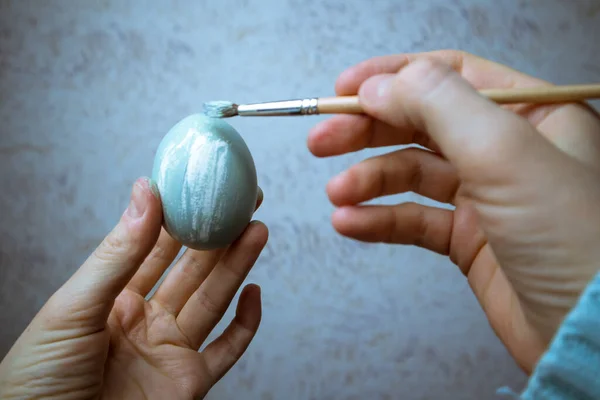 手でブラシを保持し 卵をペイント 灰色の青色の塗料でイースターの卵を描くプロセス 女性の手のクローズアップで筆をペイント 伝統と人々の概念 4月の休日 — ストック写真
