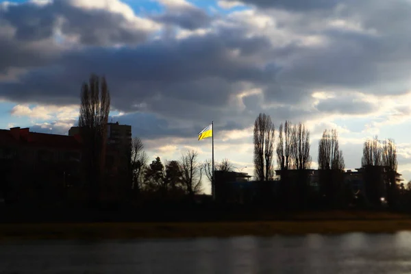 乌克兰的黄蓝国旗在阴云密布的天空中飘扬 乌克兰自由的象征 独立是希望的象征 城市景观与树木 房屋的轮廓与倾斜移位的效果 乌克兰2022年战争 — 图库照片