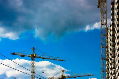 Mavi bulutlu gökyüzüne karşı inşaat vinçleri. İkametgah inşaatı. Yüksek katlı bir binanın ön cephesini donatma süreci. Apartman binası. Ticari krediler. Kule turnaları