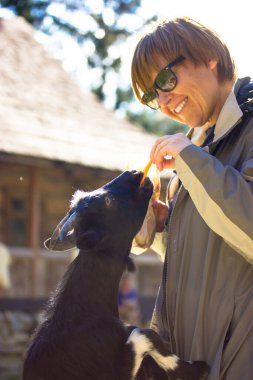 Mutlu gülümseyen kadın kara keçiyi havuçla besliyor, özel yiyecekler, çocuk odasında hayvanlara ikram ediyor, hayvanat bahçesiyle, çevre parkıyla bağlantı kuruyor. Köydeki bir çiftlikte hayvan bakımı. İnsan ve doğa etkileşimi dikey fotoğraf