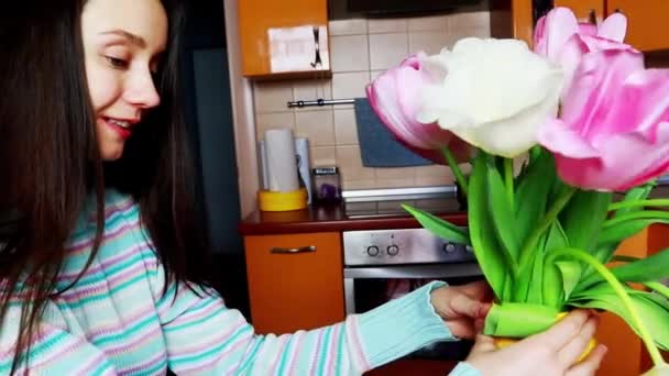 美丽的年轻女子 有着长长的黑发 在家里的黄色花瓶里欣赏着一束束春天的球状粉红郁金香花 快乐微笑的乌克兰姑娘闻到花束的芬芳 — 图库视频影像