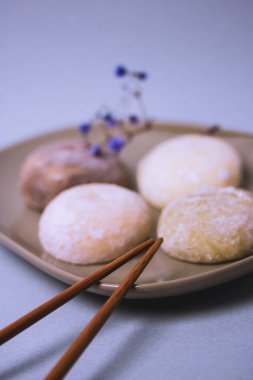Geleneksel Japon tatlı mochi 'si pirinç hamuru veya daifuku. Mochi dondurma topları ve gri tabak, mavi gri arka planda yemek çubukları. Masa ayarı. Seçici odaklanma. Yomogimochi pirinç keki..