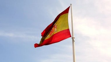 Güneşli bir bahar gününde, mavi gökyüzüne karşı, rüzgarda ıssız, büyük, kırmızı, parlak bir İspanyol bayrağı dalgalanıyor. Ulusal sembol, vatanseverlik kavramı. Yavaş çekim videosu. İspanya, Madrid ve Barselona. 