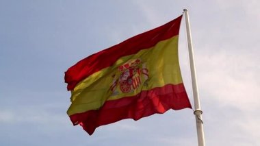 A big red yellow bright Spanish flag flutters isolated in a wind against a blue sky on a sunny summer spring day. National symbol, patriotism concept. Slow motion video. Spain, Madrid and Barcelona. 