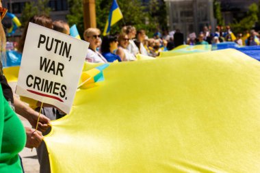 Madrid, Spain. May 8, 2022. People at rally protesting against Russian war in Ukraine holding a huge yellow blue Ukrainian flag. Poster with a text Putin war crimes. Support of Ukraine. Place for text