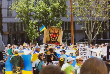 Madrid, Spain. May 8, 2022. People at rally in support of Ukrainians affected by Russia's militaries. Patriots with yellow blue Ukrainian flags. People with placards Global Boycott, Stop Putin. Murder