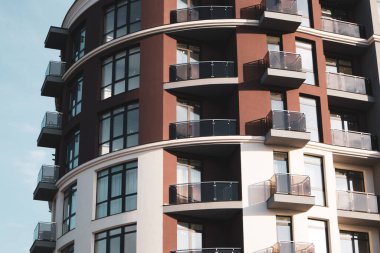 Soluk gökyüzüne karşı modern apartman kompleksi. İnşaat, emlak yatırımları, emlak piyasası konseptiyle konut satın alma. Şehir manzarası. Yüksek katlı kahverengi beyaz bina, panoramik pencereler.