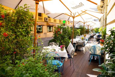 Madrid, İspanya. 9 Mayıs 2022. Boş bir kafe, yemyeşil bir bitki örtüsünün ortasındaki şehir ortamında bir restoran terası. Oturma, konuklara servis edilen eski masa ve sandalyeler. Masa örtüleri üzerinde tablo takımı. 