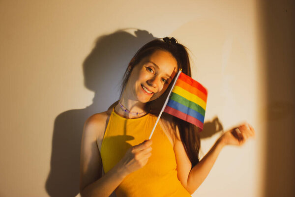 Красивая молодая женщина, девушка с флагом ЛГБТ в руке празднует месяц Прайда. Симпатичная сексуальная девушка веселится, улыбается, смеется. Rainbow flag - a symbol of lesbians, bisexuals, pansexuals, gays. Выхожу..