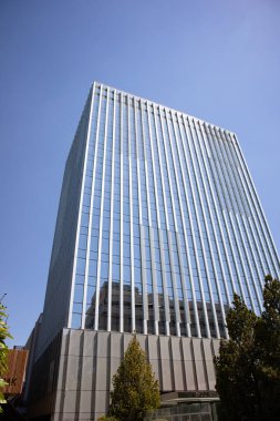 Yazlık şehirde mavi gökyüzüne bakan aynalı camlarla dolu modern, çok katlı bir bina. Konut ya da ofis binası. İnşaat işi. Gayrimenkul. Şehir manzarası. Şehir manzarası.