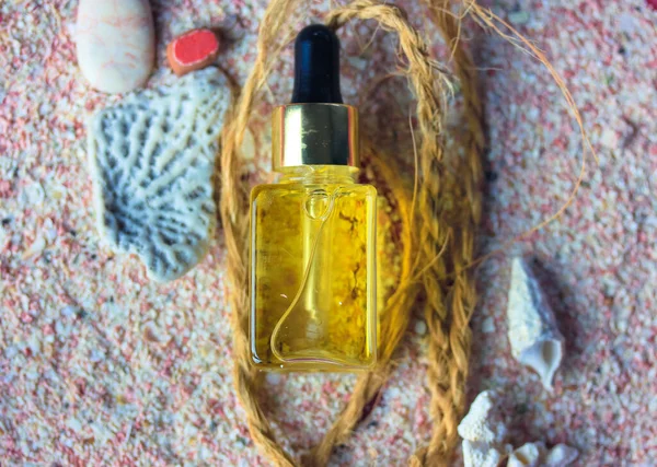 Yellow oil serum essence in glass bottle flatly. Concept of natural cosmetic, trendy beauty skin care. Sunscreen oil to protect the face body at summer days. Sea theme, seashells, stones, pink sand.