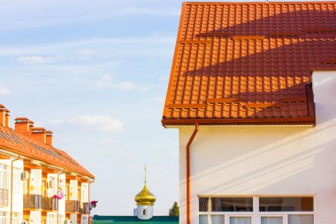 Yeni beyaz apartman cephesi, mavi gökyüzüne karşı kırmızı terracotta kiremit çatı. Bahçesinde bir kilise olan yeni inşa edilmiş modern konut alanı. Gayrimenkul yatırım kavramı. Ev detayı