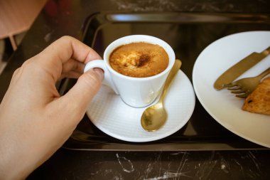 Bir kadının elinde küçük seramik ya da porselen beyaz bardakta sıcak kahve - espresso, cappuccino, mochaccino. Kahvaltı, bir kafede kahvaltı, bir restoran. Kahve fincanı siyah mermer bir masada tepside.