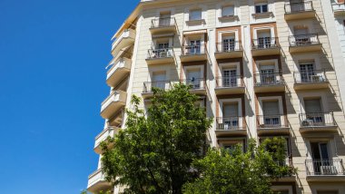 Madrid, İspanya. 1 Haziran 2022 Beyaz Tarihi Konut Apartmanı köşesi. Şehir çevresindeki yüksek binalar ve yeşil ağaçlar. Şehir caddesinde modern mimari mavi gökyüzüne karşı.