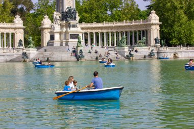 Madrid, İspanya. 9 Mayıs 2022. Bir aile - anne, baba, iki oğul - yaz tatillerinde Retiro Park 'taki büyük bir gölette mavi bir teknede yüzüyorlar. İnsanlar XII. Alfonso Anıtı 'na karşı. Dışarıda rahatla..