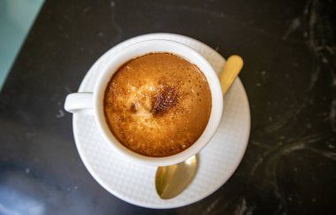 Beyaz kahve fincanı ve kokulu içecek. Sütlü Americano veya kahverengi köpüklü kapuçino. Siyah mermer masa manzaralı. Kahvaltı için sıcak bir içecek, öğle yemeği, kafe, restoran şubesi. Tablo takımı.