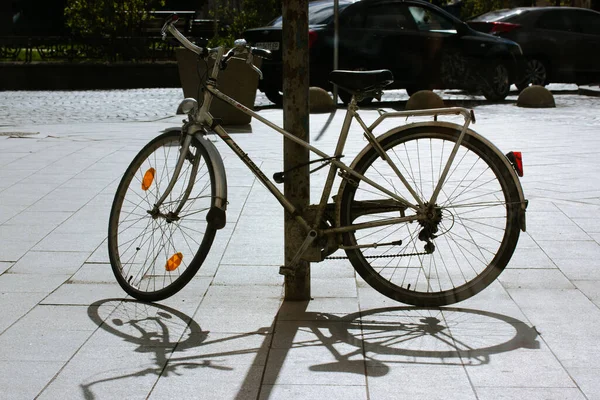 Uzhgorod Ukraine. April 1, 2022. An old retro bicycle stands parked on sidewalk, contrasting shadow on sunny day. Ecology urban transportation. Wheels, tires, spokes of cycle bike leaning against pole