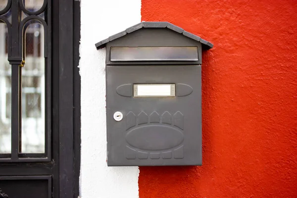 Metal grey mailbox, postbox on red and white wall. A box for letters, correspondence delivered to a home address in an apartment building. The exterior of a private house. Traditional letters delivery