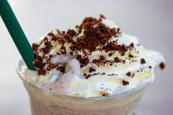 Frappe with cookie crumb, whipped cream, chocolate crumbs in plastic glass with green paper tube. Icy drink refreshing for hot summer day. Macro photography of non alcoholic drinks, cold milkshake.