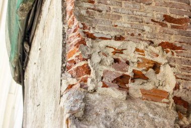 Tamire ihtiyacı olan eski bir tuğla binanın köşesi. Yerleşim yerinin yenilenmesi gerekiyor. Tamir işleri, inşaat şebekesi. Kırmızı tuğlalı Grunge duvarı soyut bir arkaplan. Tuğla dokusu
