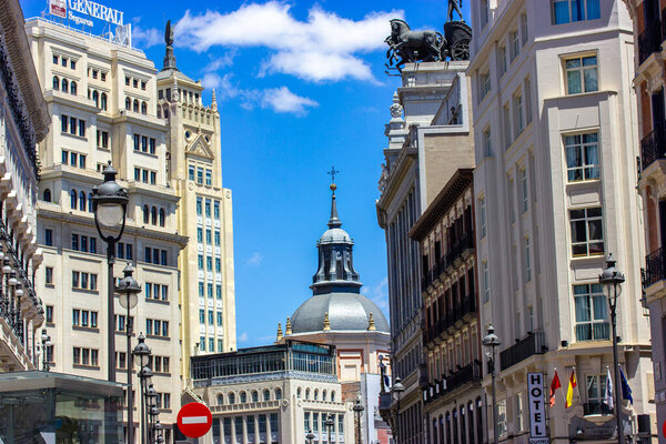 Madrid, Spain. June 1, 2022. Ancient old vintage architecture in a modern city center. Universal bank building, hotel sign, road signs in urban scene. A dome of a church on a horizon against blue sky.