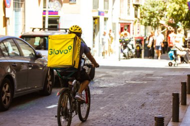 Madrid, İspanya. 1 Haziran 2022. Glovo kuryesi. Bisikletli bir teslimatçı, sarı sırt çantalı bir bisikletle şehir caddesinde bir müşteriye yiyecek getiriyor. Şehir fast food 'u. Müşteriye sipariş iletiliyor.
