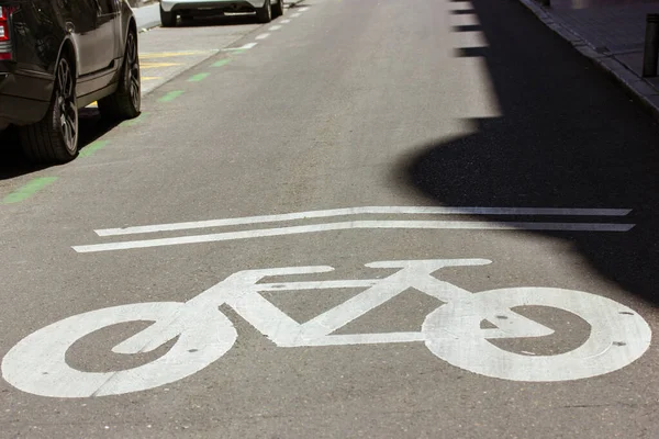 White bicycle sign, symbol, pictogram painted on paved bike path in urban environment. Urban street with a convenient infrastructure for mobility, active leisure. Bike commute on pavement. Bikes lane.