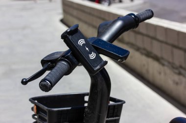 Gidonun üzerinde elektrikli bisikletin şarj levhası olan bir cep telefonu tutucusu. Kentsel bir ortamda taşınmak. Spor ve şehir dışı aktiviteleri. Sepetli bisiklet. Kiralık çevre dostu ulaşım