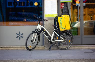 Madrid, İspanya. 1 Haziran 2022. Siparişler için sarı sırt çantalı iki tekerlekli beyaz bir bisiklet bir şehir caddesinde park edilmiştir. Fast food teslimatı. Şehir yaşam tarzı. Gıda ve bakkal Glovo dağıtım servisi.