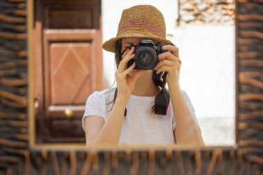 Madrid, İspanya. 1 Haziran 2022. Hasır şapkalı kız fotoğrafçı ve Canon kamera. Kadın yolcuların tam boy yaratıcı oto-portre fotoğrafları. Şehrin sokaklarında bir kadın aynada kendini vuruyor.